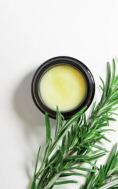 solid cosmetic oil with rosemary extract in a glass jar and fresh rosemary branches on a white background, top view